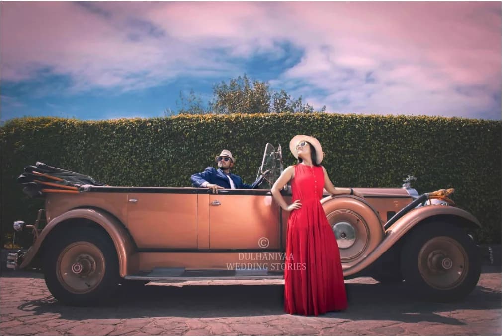 Couple posing with a vintage copper convertible under a pink sky