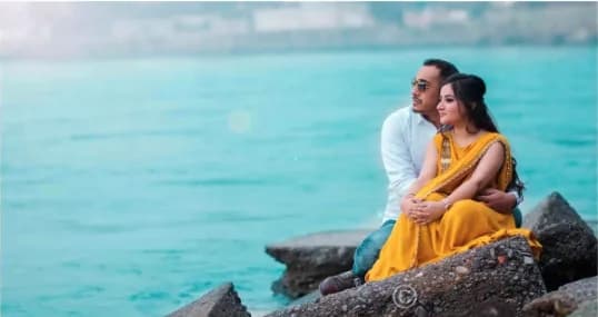 Couple in white and yellow sitting on rocks by turquoise water