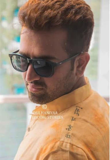 Groom in sunglasses and a haldi-stained kurta looking over his shoulder